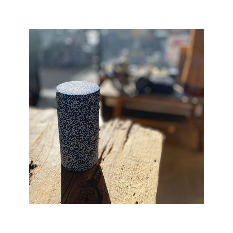 Cylindrical box in washi paper with white flower pattern on blue background placed on light wood table