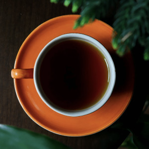 Tasse Pu-Erh Schwarztee in einer orangefarbenen Tasse auf einem Holztisch