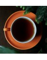 Tasse Pu-Erh Schwarztee in einer orangefarbenen Tasse auf einem Holztisch