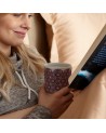 Donna che tiene una tisaniera Andalusia Berry con motivi colorati mentre legge un libro a letto