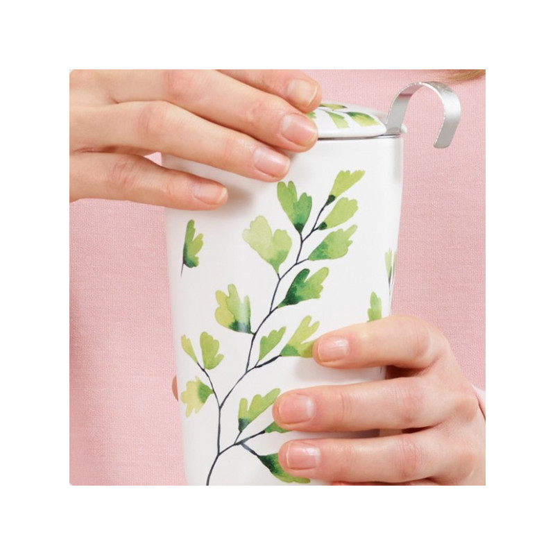 Witte theemok met groene ginkgo-bladmotieven met deksel vastgehouden door twee handen
