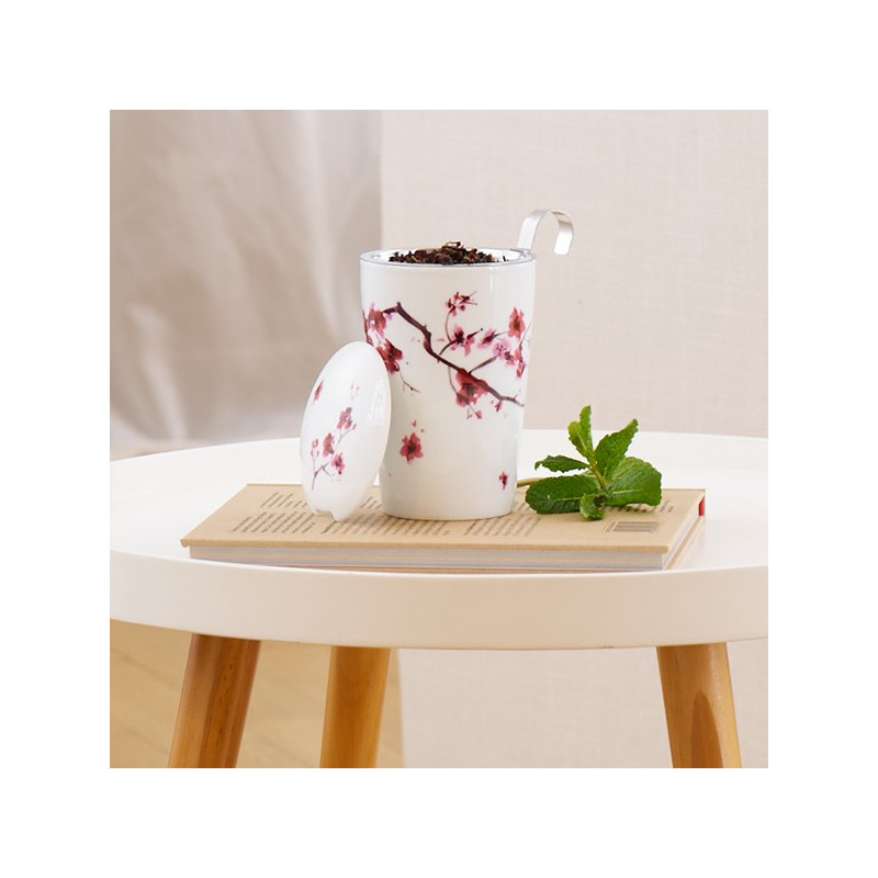 Tazza infusore in porcellana con motivo fiori di ciliegio contenente infusione e cucchiaio metallico su libro