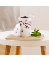 Tazza infusore in porcellana con motivo fiori di ciliegio contenente infusione e cucchiaio metallico su libro