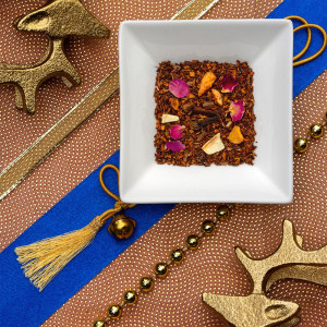 Mischung aus Rooibos mit Rosenblütenblättern und Zitrusfruchtstücken auf festlichem Hintergrund mit goldenen Dekoelementen