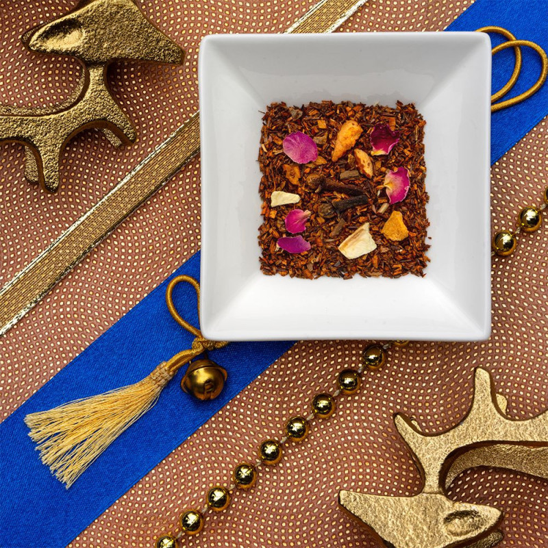 Mischung aus Rooibos mit Rosenblütenblättern und Zitrusfruchtstücken auf festlichem Hintergrund mit goldenen Dekoelementen