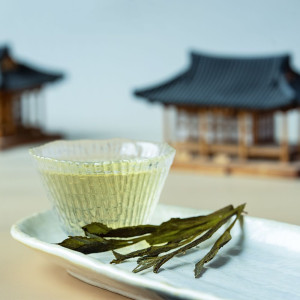 Clear infusion of Tai Ping Hou Kui tea with long flat leaves on white tray