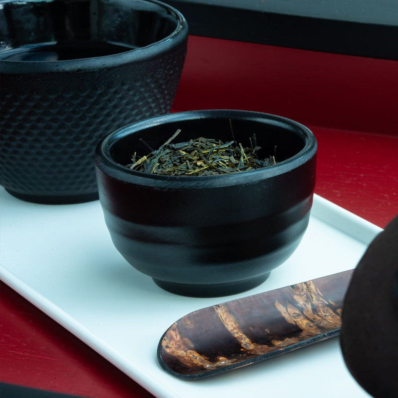 Sencha groene thee gedroogde bladeren in zwarte kom met houten lepel op wit plateau