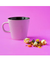 Weiße Tasse mit Kräutertee-Aufguss „Mandelwolke“, getrocknete Früchtestücke und Popcorn auf rosa Hintergrund