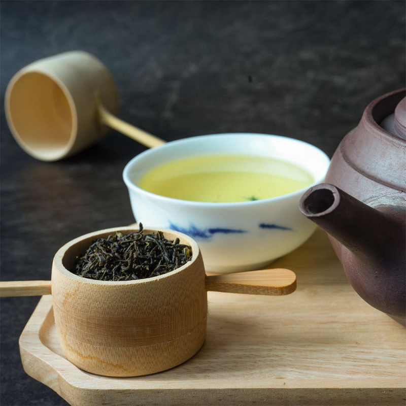 Groene thee droge bladeren in houten bakje kopje opgetrokken thee aarden theepot op houten dienblad