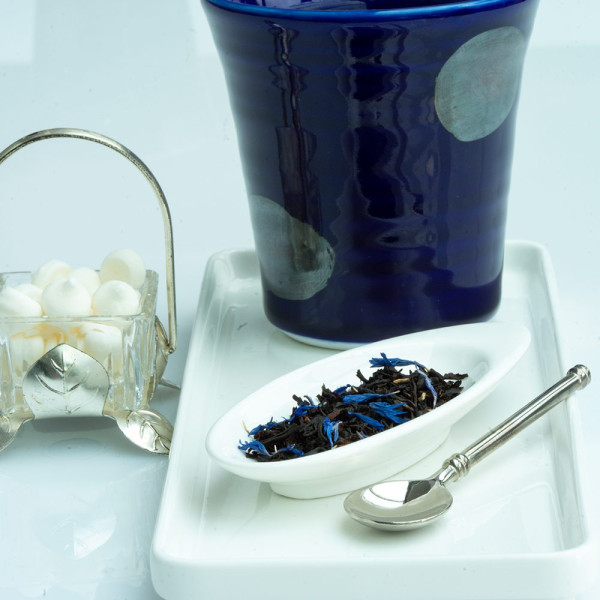 Foglie di tè nero Blue Earl Grey con fiori blu su cucchiaio bianco e tazza blu