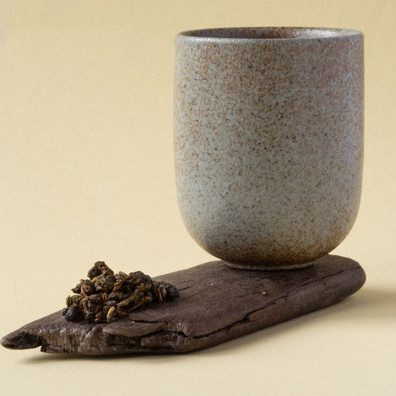 Beige ceramic cup placed on wooden board with rolled Oolong Java Halimun Jade tea leaves