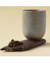 Beige Keramiktasse auf Holzbrett mit gerollten Blättern des Oolong Java Halimun Jade