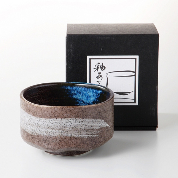 Brown matcha bowl with white pattern and blue interior accompanied by a black box