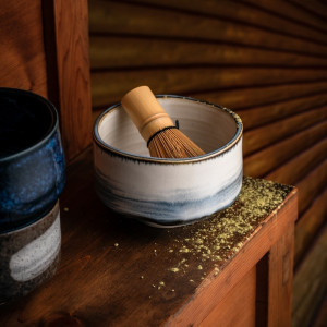 Weiß-blaue Keramikschale mit Bambusbesen zur Matcha-Zubereitung auf Holztisch