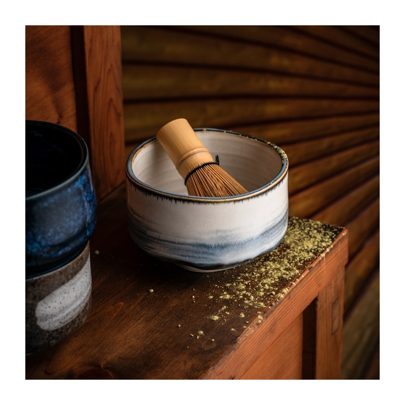 White and blue ceramic bowl with bamboo whisk for matcha preparation placed on wooden table