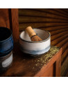 White and blue ceramic bowl with bamboo whisk for matcha preparation placed on wooden table