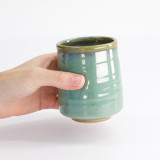 Kinyo keramische groene kop met beige rand vastgehouden in een hand