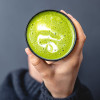 Cup of frothy vanilla matcha held by a hand on grey background