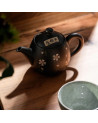 Teiera Tokoname nera decorata con fiori bianchi su tavolo in legno con tazza in ceramica verde