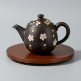 Tokoname black teapot decorated with white flowers placed on a round wooden tray