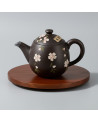 Tokoname black teapot decorated with white flowers placed on a round wooden tray