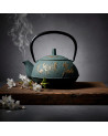 Green cast iron teapot with butterfly and embossed flowers black handle on smoked wooden board