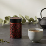 Mandala Ebony black tea caddy with red floral patterns on black background next to a steaming cup of tea