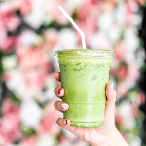 Kunststoffbecher mit gefrorenem Erdbeer-Matcha-Latte und Strohhalm, gehalten von einer weiblichen Hand