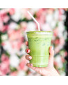 Kunststoffbecher mit gefrorenem Erdbeer-Matcha-Latte und Strohhalm, gehalten von einer weiblichen Hand