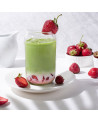 Glas Matcha-Latte mit Erdbeere, Erdbeerstücken und Eiswürfeln auf weißem Teller