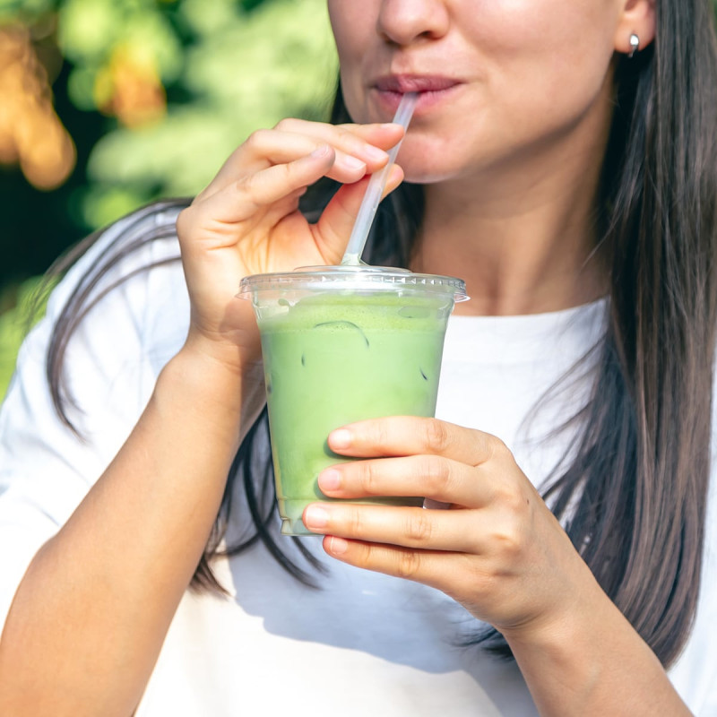 Woman holding plastic cup of iced vanilla matcha latte with straw outdoors