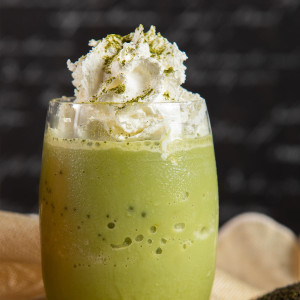 Matcha-Latte mit Haselnussschokolade, Schlagsahne und grünem Teepulver in einem transparenten Glas