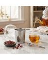 Stainless steel tea infuser placed on a table with herbal tea in a glass cup and glass teapot in the background