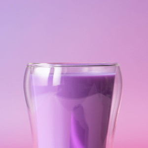 Glas paarse ube-latte op roze achtergrond – Thés & Traditions