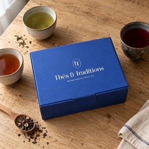 Coffret Découverte Thés & Traditions : écrin bleu sur une table en chêne, entouré de trois tasses de thé de couleurs différentes