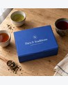 Coffret Découverte Thés & Traditions : écrin bleu sur une table en chêne, entouré de trois tasses de thé de couleurs différentes