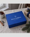 Coffret de Noël Thés & Traditions : écrin bleu sur une nappe en lin, avec branche de sapin, cannelle et paquet cadeau