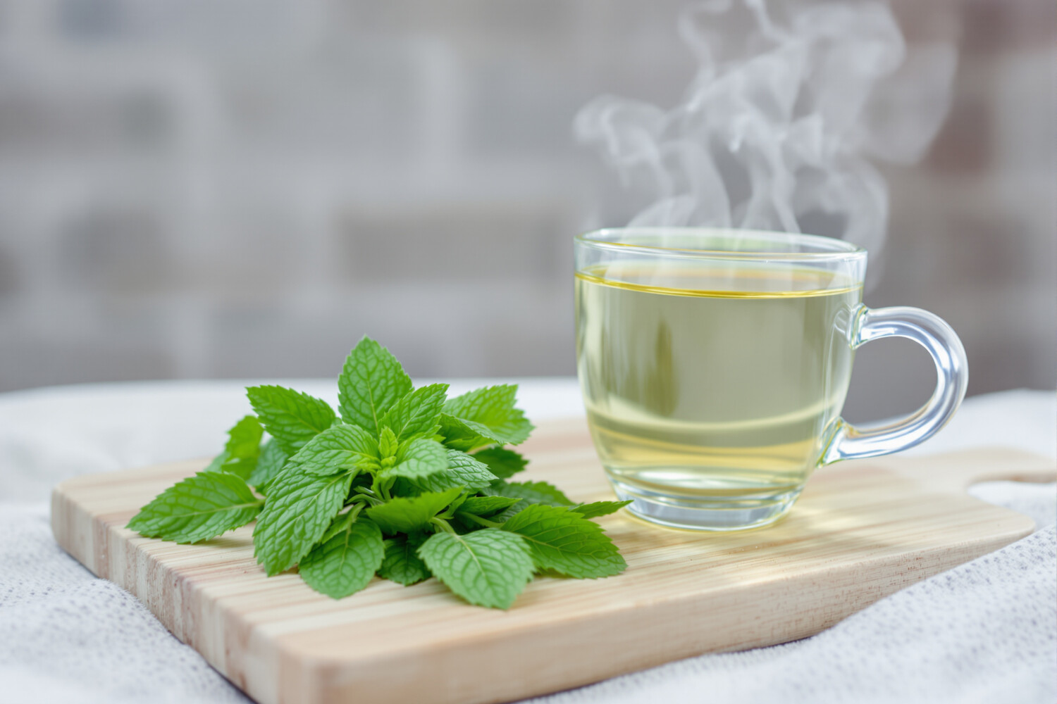 Feuilles de menthe poivrée fraîche et tasse d'infusion claire sur planche en bois