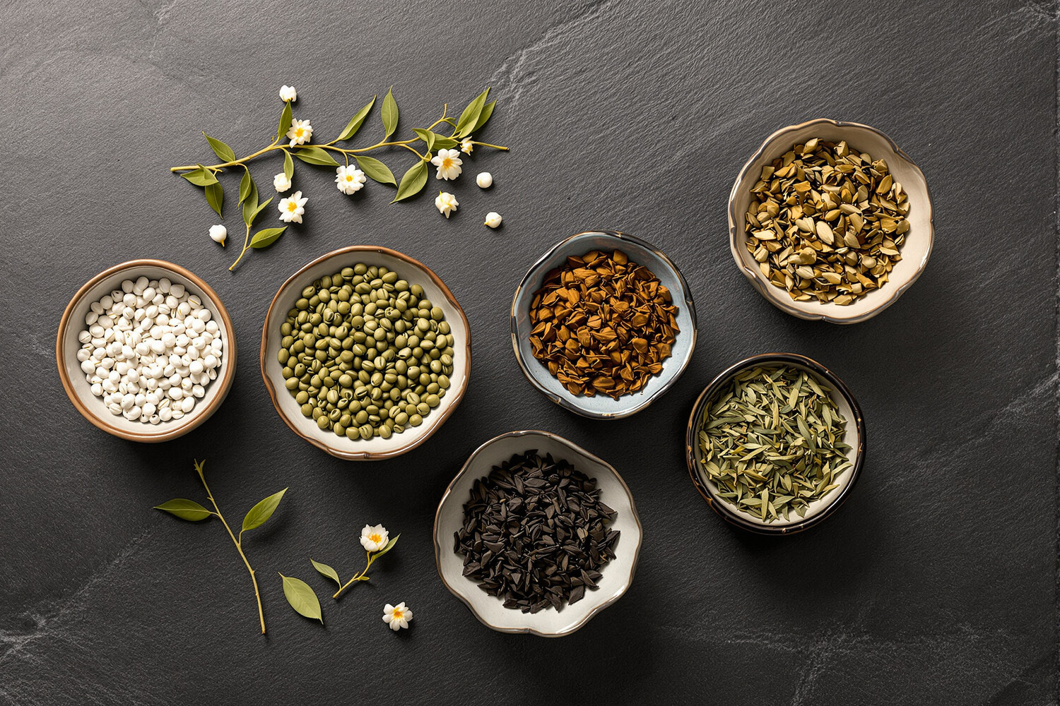 Five ceramic bowls holding different varieties of loose-leaf teas for cold brew, seen from above on a slate surface.